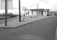 A scene of peace and tranquility at Barassie in August 1963. With the time at just after quarter past one on the station clock, a member of staff tends flower beds on the Kilmarnock platform.<br><br>[Colin Miller 11/08/1963]