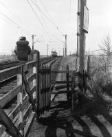 Looking west from Geilston level crossing, Cardross, in March 1974 as a Class 303 unit disappears into the distance towards Helensburgh. Note the LNER lamp housing on top of the gate.<br>
<br><br>[John McIntyre /03/1974]
