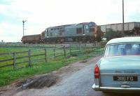 A smart looking Austin Cambridge is held at the level crossing at Cowpen Bewley, to the north east of Billingham in the 1960s, as a class 37 with brake-tender attached rumbles past with a coal train  heading for Teesside.<br>
<br><br>[Bruce McCartney //]