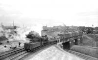 Ivatt class 2MT 2-6-0 no 46455 brings a freight out of Crown Street goods depot, Carlisle, in July 1958 across a double track bridge spanning 3 sets of lines. Those nearest are the goods lines from Upperby, in the centre are those from London Road and furthest away are the N&C/S&C passenger lines into Citadel station. The WCML can be seen on the extreme left of the picture. Although best known as a goods depot, Crown Street began life in 1844 as the site of the passenger terminus of the Maryport & Carlisle Railway, a function it performed for only 5 years, following which trains switched to Citadel. Crown Street goods depot lasted much longer however, being officially closed as such in 1966, although most of the track had been lifted the previous year. The deck of the bridge in the photograph had been removed by 1971. [See image 5345]  <br>
<br><br>[Robin Barbour Collection (Courtesy Bruce McCartney) 05/07/1958]