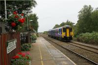 A stopping eastbound service from Southport to Manchester Victoria slows for Bescar Lane station in West Lancashire on 26 August 2009. The station has received a lot of attention from the station adoption group with very attractive and colourful display of flowers on both the Southport platform and, behind the camera, the Manchester platform on the other side of the level crossing.<br><br>[John McIntyre 26/08/2009]