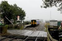 A very wet afternoon at Hoscar station as a Southport to Manchester service rushes through on 26 August 2009. The train is not stopping at this rural station and the level crossing barrier is already lifting to allow road traffic to move on Hoscar Moss Road. Just out of shot to the left of the photo is the Railway public house, a very useful place to retreat to on such a miserable day!<br><br>[John McIntyre 26/08/2009]