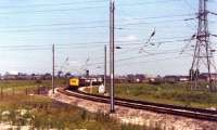 This photograph was taken looking back from a Glasgow to London train as it passed Farington Junction in June 1976. Waiting to join the WCML southbound on the curve from Lostock Hall Junction is a Class 40 and a dead electric locomotive on a freight train. Today the area to the left and right of the Class 40 is covered with housing.<br><br>[John McIntyre /06/1976]