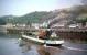 A fine looking Clyde 'puffer' heads west past Bowling Harbour in the late 1950s with the entry to the Forth and Clyde Canal out of shot to the right. The photograph is probably taken from one of the Clyde passenger steamers. A long train looks to be coasting into Bowling (NB) station in the background and to the right a freight train is in the small quayside yard, with its travelling cranes, at the east end of Bowling Harbour. These sidings were accessed by both the NB (from the west) and Caley (from the east). The Caley approach involved a swing bridge over the canal to the south of, and at a lower level to, the substantial but disused railway swing bridge which is still in place. The main Caley line cannot be seen in this view but was on the wooded hillside above the NB line. The wooden quay seen here no longer exists although its remains can be seen at low tide.<br>
<br><br>[A Snapper (Courtesy Bruce McCartney) //]