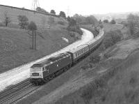 The Harwich Parkeston Quay - Manchester Piccadilly boat <br>
train, hauled by 47047, is nearing the end of its journey as it passes through Buxworth cutting, about a mile and a half to the west of Chinley station, in June 1977. The train is formed of early Mk II stock and no doubt a Mk I buffet (in the early seventies it had been one of the last services to employ a Gresley buffet car).<br><br>[Bill Jamieson 11/06/1977]