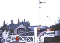 Looking over the level crossing at Cantley, Norfolk, as the gates are reopened in January 1988 with a DMU standing at the platform. View is north west towards Norwich. <br><br>[Ian Dinmore 13/01/1988]
