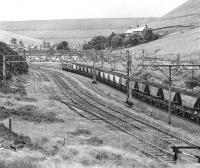 The hamlet of Dunford Bridge is dominated by Winscar Reservoir in the background. It is also evident that an extensive track layout survived here until closure, although it is doubtful whether either the loops or sidings saw much use by this stage. 76007+76012 are passing westbound on 17 July 1981 with coal for Fiddler's Ferry power station.<br><br>[Bill Jamieson 17/07/1981]