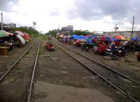 Market day at Taguig, right next to the PNR main line to Alabang [see image 40401]. Notice the market stalls built onto motorbike sidecars; the practical addition of umbrellas; and the skate (in the distance) on the right hand track. Skates are home-built powered wagons, privately owned and operated. They provide a useful service to the public, but contribute nothing to PNR; and can be rather dangerous, as they have no formal collaboration with the PNR working timetable. Understandably, they are not easy to photograph; especially up close.<br><br>[Ken Strachan 28/08/2012]