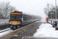 A northbound service pulls into Stonehaven station with easterly gale force winds driving snow in from the north sea on Sunday 10th March 2013. A Scotrail staff member is hard at work clearing snow and salting the platforms. <br><br>[Brian Taylor 10/03/2013]