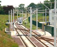 An eastbound Edinburgh tram approaching the short platforms at the staff halt alongside the south wall of Gogar tram depot on 10 June 2013. The gate from the platform on the right gives direct access into the depot. The tram in the picture is being routed back into the yard following a training trip to the airport.<br><br>[John Furnevel 10/06/2013]