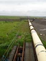 View west from the A99 near Keiss, Caithness, showing the 7.5km narrow gauge track used to move welded sections of pipeline. Completed lengths are sealed and hauled out into Sinclairs Bay by tug. The system appears to be out of use at present, despite there being near 2km of welded pipeline visible on rail mounted cradles between the welding station and the hilltop. Pipe sections are moved along the track using cable haulage.<br><br>[David Pesterfield 22/06/2013]