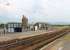 Three items of interest in this view of Seascale's southbound platform. The old Furness Railway water tower is a prominent local landmark. To its right is the old goods shed, which is now the town's Sports Centre. On the platform itself is a <I>Harrington Hump</I> which provides level access to trains. These were pioneered at the station of the same name, just north of Whitehaven, and provide a cost effective alternative to raising low platforms along their full length. They are appearing at various Cumbrian Coast stations and elsewhere in the UK. <br><br>[Mark Bartlett 27/07/2013]