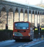 The 12.45 ex-Gorebridge is held at the B6482 junction waiting to join the A7 shortly after calling at Newtongrange on 8 January 2013. The no 29 Lothian bus is heading for Silverknowes. A section of Newbattle Viaduct, lit by harsh winter sunshine, dominates the picture.<br><br>[John Furnevel 08/01/2013]