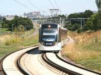Shortly after leaving Balgreen on a sunny 25 July a westbound Edinburgh tram climbs to cross the Edinburgh - Glasgow main line on the approach to the flyover at Saughton. <br><br>[John Furnevel 25/07/2014]