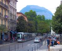 TAG Alstom Citadis 402 tram 6021 is one of a batch of 35 introduced to Grenoble in 2005. Here it is, dwarfed by a nearby Alp, and westward bound on a Line B service into Place Notre Dame in July 2014. It will  head into the city centre and on to its terminus at the Palais de Justice. This line is currently being extended into the north west of the city to serve the scientific community centred on the European Synchotron Radiation Facility.<br><br>[Andrew Wilson 04/07/2014]