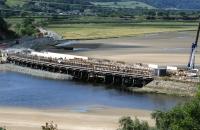 The soon-to-be-demolished original Pont Briwet on 6th July with its replacement taking shape alongside. Work on the new bridge caused the 1860s wooden trestle bridge to become unstable in December 2013, following which the line was closed from Harlech to Pwllheli. It is expected to reopen by September 2014. [See image 46693]<br><br>[Colin McDonald 06/07/2014]