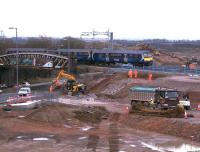 A Motherwell - Milngavie service approaches the site of the new Braehead viaduct on 6th March 2015. The temporary embankments and retaining wall of gabion baskets at the side of the railway line are nearing completion. Piling work for the replacement M8/Bredisholm Road overbridge is underway off picture to the right. Rail services should be unaffected by the works until the planned closure in July. <br><br>[Colin McDonald 06/03/2015]