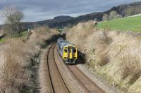 The 1426 Carlisle to Leeds service, formed of two Class 158s, approaches the footbridge at Langcliffe just north of Settle on Easter Saturday 2015. Pen-y-ghent is prominent in the background above the general landscape of the Ribble Valley.  <br><br>[Mark Bartlett 04/04/2015]