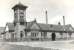 The road approach to Ardrossan North station, viewed from the south east on 24 May 1960. The tall chimneys in the background are part of the large Shell refinery on the west side of the line [see image 23867]. By this time the station had been closed to passengers for some 28 years (July 1932). Demolition of the building would be completed by 1965, with the site subsequently used for lorry/coach parking.<br><br>[G H Robin collection by courtesy of the Mitchell Library, Glasgow 24/05/1960]