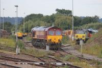 DBS 66200 eases out of the stabling sidings in Westbury Yard on 25th July 2015. To the right, Colas 70810 stands at the head of a line of stabled Class 70 and Class 66 locos in this view taken from the station platform.<br><br>[Mark Bartlett 25/07/2015]