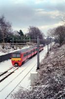 320.307 passes the site of Milngavie signalbox early in 1991. The line had recently been singled, thus the approach 'wrong line' to the station, and snow can be seen on the disused rails to the right.<br><br>[Ewan Crawford //1991]