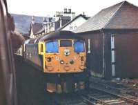 Kyle line services cross at Achnasheen in 1977. Viewed from a BRC&W Class 26 hauled westbound service, a classmate heading for Inverness is seen. Alongside the loco is the now demolished goods shed with the station hotel (later burnt down) behind. <br><br>[Mark Bartlett 13/09/1977]