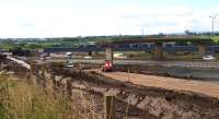  Partly obscured by the remaining spans of the former Bredisholm Road bridge over the A8, a diverted Class 170 DMU speeds across the Bargeddie Bridges. In the foreground the new alignment for the A8 takes shape; the new section of the M8 will run alongside it, cutting through the present dual carriageway after passing under the new railway viaduct opened in 2015 [see image 46140].<br><br>[Colin McDonald 29/07/2016]