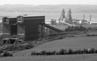 Looking over Hunterston Import Terminal. One bunker was for coal, the other for iron ore. In the background the Midrex direct reduction plants can be seen - never used and later sold, dismantled and reassembled in the United States. (Now said to be in Saudi Arabia). It was to access this that the low level siding was built.<br>
<br>
An EMU can be seen on the Largs branch.<br><br>[Bill Roberton //1992]
