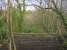 View south east over the safety parapet built across the solum at the remaining abutment of the Calderpark viaduct. The photograph looks over the North Calder Water, along the line taken by the viaduct and towards Maryville station. Hidden in the trees but just discernible in the gap, slightly left of centre, are the stables since built on the alignment of the railway.<br><br>[Colin McDonald 20/02/2017]