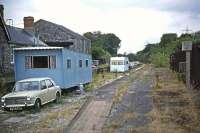 A peculiar queue of abandoned caravans and cars stretches along the track bed of the former Taunton-Barnstaple line at Bishops Nympton and Molland station on 11th September 1976. It was as if holiday motorists had tried to use the disused railway as an alternative to the congested roads and come to grief. Substantial holiday traffic had indeed come this way in the past, but on rails until the line closed in 1966. [Ref query 1125]<br><br>[Mark Dufton 11/09/1976]