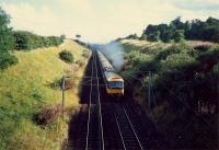Approaching Mossend Marshalling Yard from the north is a 47 hauled passenger train. It is about to pass under the A8.<br><br>[Ewan Crawford //1987]